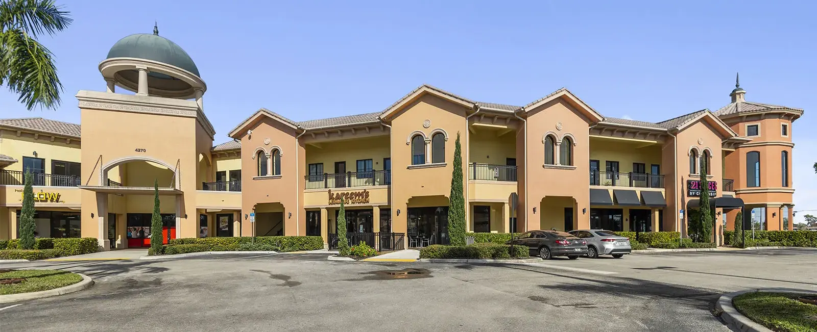 Ground-level view of Sugden Park Plaza in Naples, Florida, featuring storefronts, pedestrian walkways, landscaping, and commercial tenant spaces.